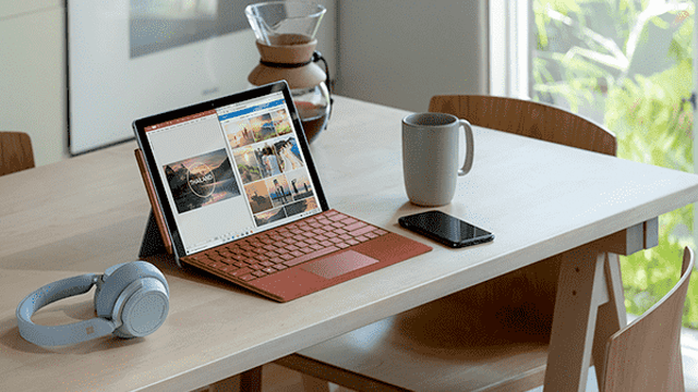Table blanche avec ordinateur portable, tasse, téléphone, casque. Carafe en verre en arrière-plan.