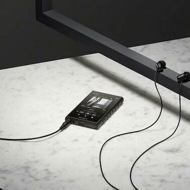 Lecteur noir connecté à des écouteurs sur une surface blanche, avec un cadre noir en arrière-plan.