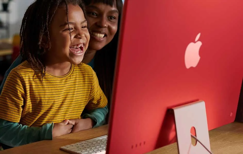 Een rode iMac staat op een houten tafel, met een wit Apple-logo. Een toetsenbord staat voor de computer.
