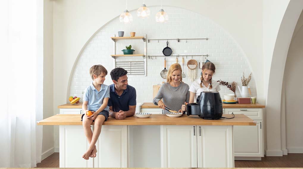 Een keuken met een houten aanrecht, witte kasten en rekken. Een zwarte airfryer staat op het aanrecht.