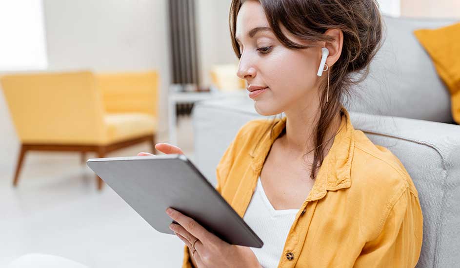 Een grijze tablet wordt vastgehouden tegen een achtergrond van een gele stoel en een grijze bank.