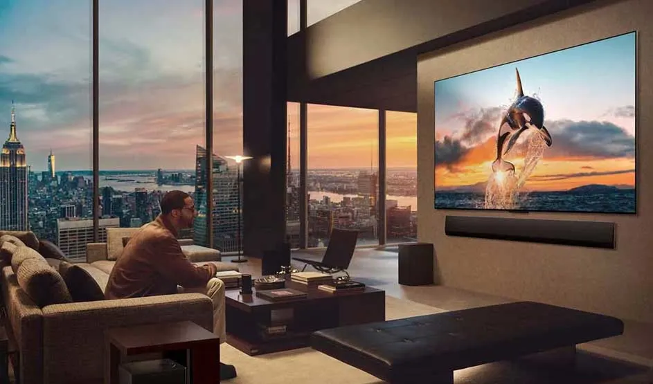 In een luxe woonkamer kijkt een man naar een groot scherm met een springende orka, terwijl de stad bij zonsondergang zichtbaar is.