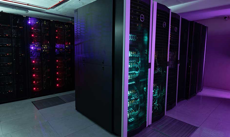 Un centre de données avec des rangées de baies noires, des voyants colorés et une lumière violette dans une salle technique.