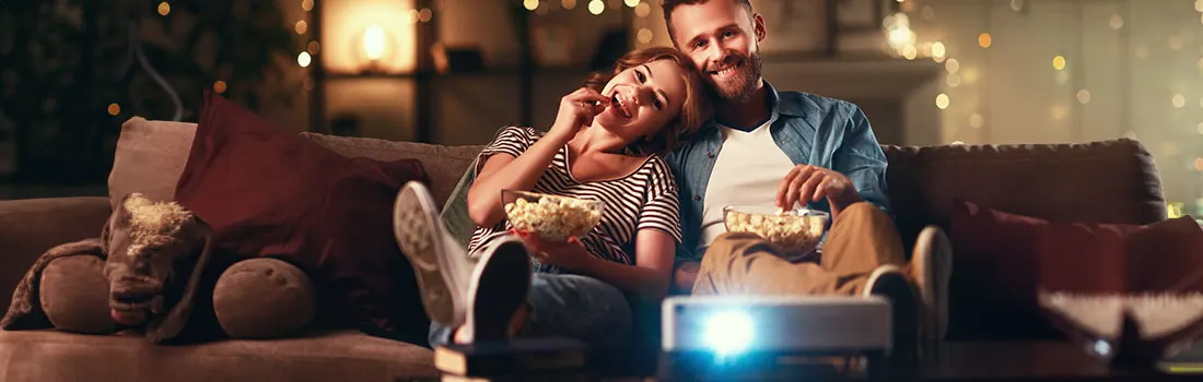 A projector shines on a couch with popcorn, pillows and lights.