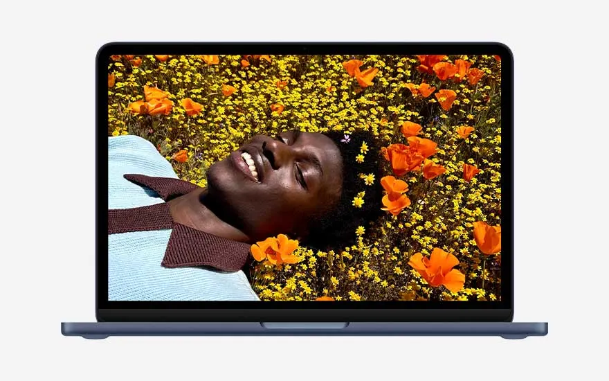 L’écran d’un MacBook affiche une personne souriante allongée dans un champ de fleurs orange et jaunes éclatantes, avec des couleurs riches et nettes.