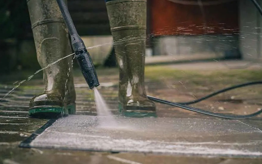 Close-up van iemand die betonnen tegels reinigt met een hogedrukreiniger, waarbij de krachtige waterstraal vuil wegspuit van het oppervlak.