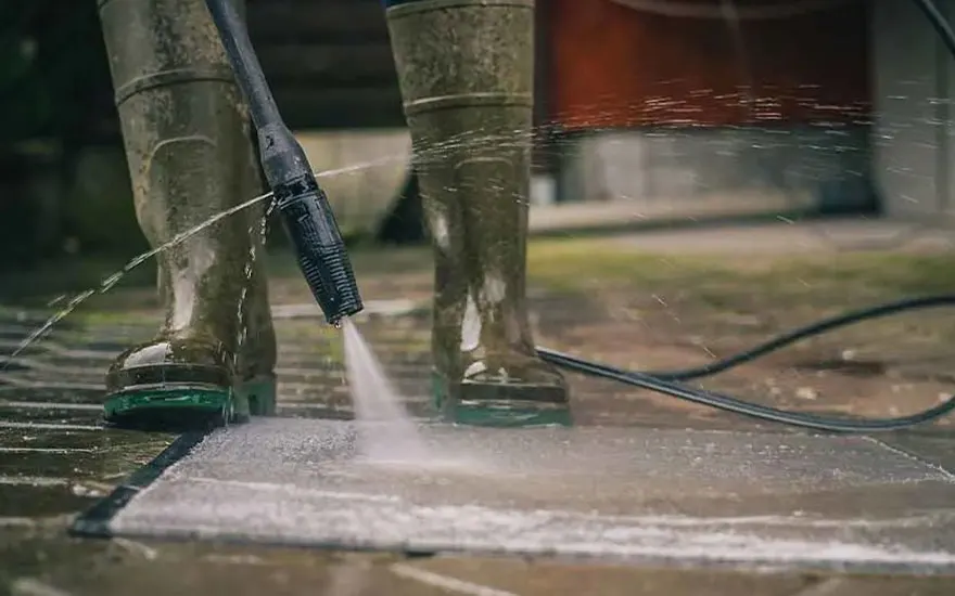 Close-up van iemand die betonnen tegels reinigt met een hogedrukreiniger, waarbij de krachtige waterstraal vuil wegspuit van het oppervlak.