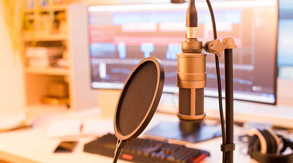 Gouden microfoon met popfilter op standaard voor een computerscherm met audiobewerkingssoftware, op een wit bureau.