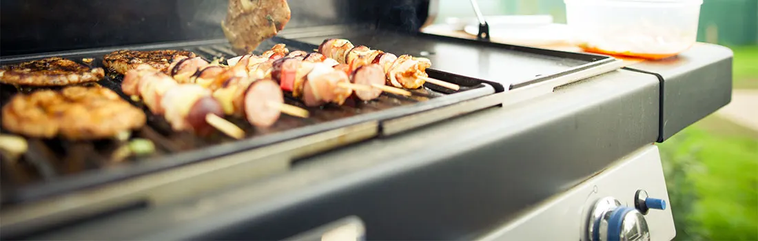 Barbecue gris avec brochettes et galettes en cuisson. Arrière-plan vert avec récipient.
