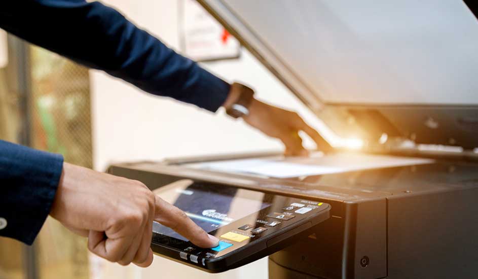 Een zwarte printer met een open scannerdeksel. Iemand bedient het touchscreen. Papier is zichtbaar in de scanner.
