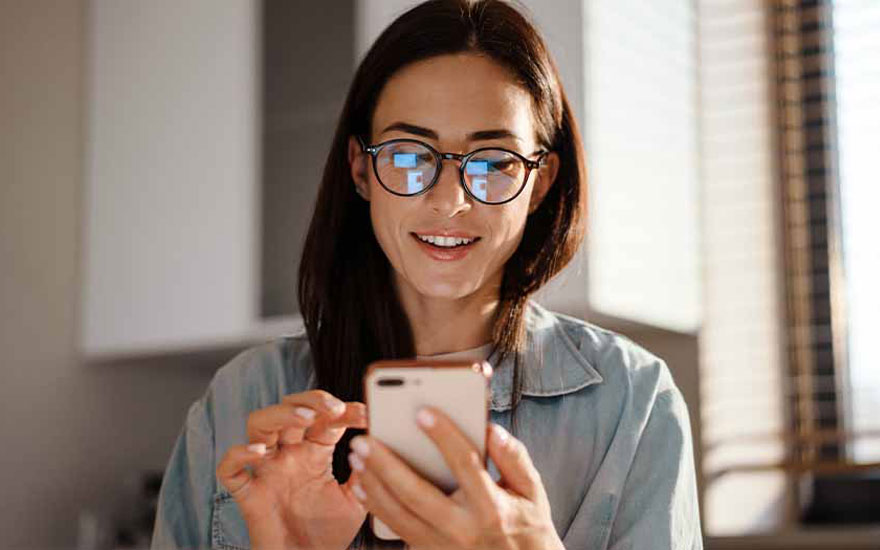 Une personne utilise un smartphone couleur or dans une pièce avec des armoires blanches et des stores.