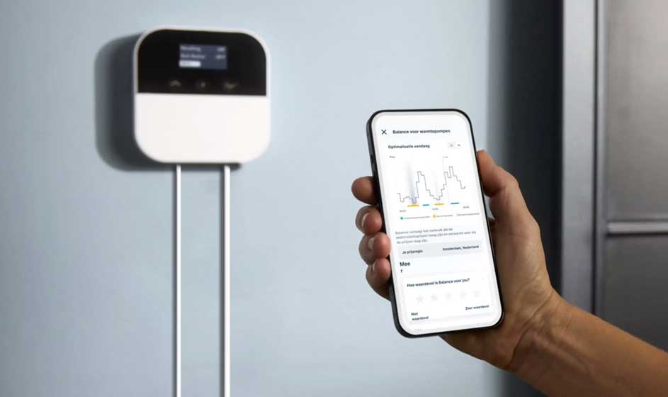 Un appareil blanc fixé au mur se trouve près d’un smartphone. Une main tient le téléphone, dont l’écran montre un graphique et plusieurs données.
