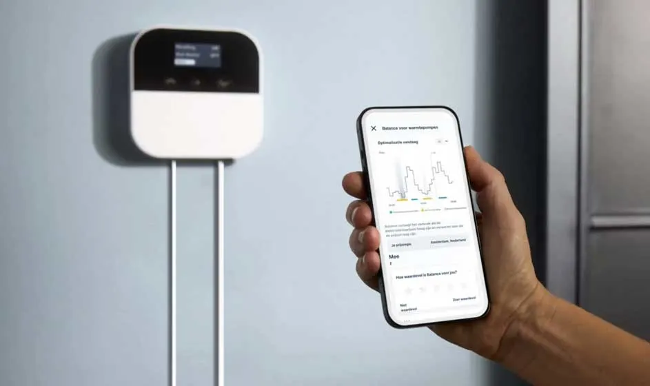 Un appareil blanc fixé au mur se trouve près d’un smartphone. Une main tient le téléphone, dont l’écran montre un graphique et plusieurs données.