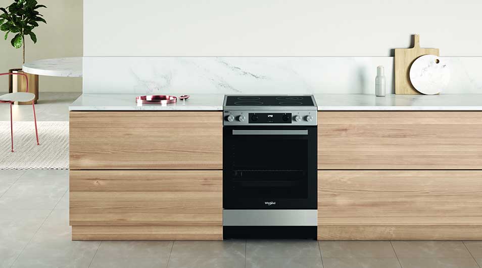 Een keuken toont een roestvrijstalen fornuis tussen houten kasten onder een wit aanrecht.