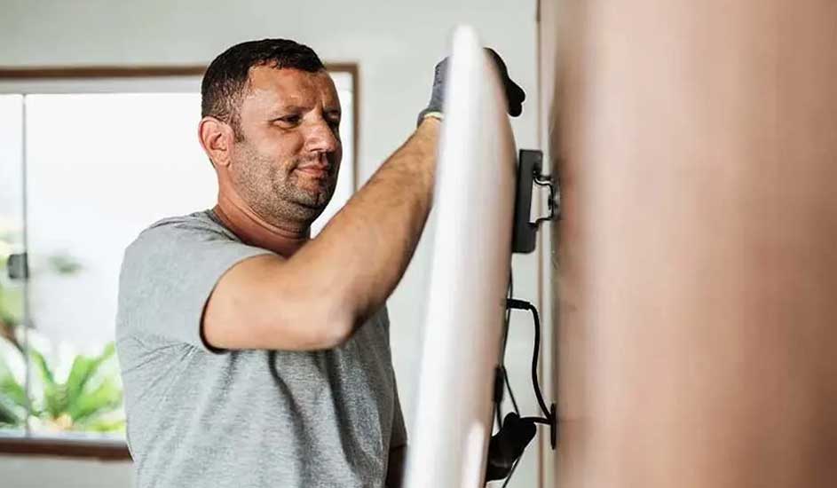 Iemand monteert een flatscreen-tv aan de muur in een lichte kamer, met handschoenen aan voor bescherming. Merk is niet zichtbaar.