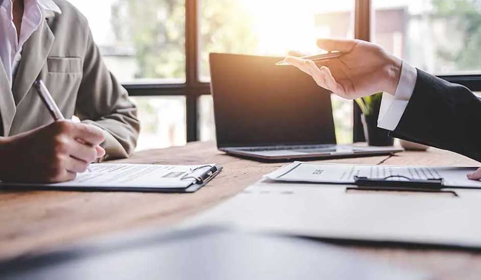 Sur une table en bois, un ordinateur portable est ouvert, avec des documents et des stylos.