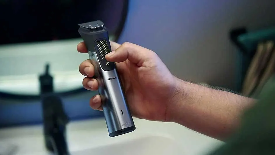 Une main tient une tondeuse Philips argentée avec des accents noirs, devant un lavabo blanc dans une salle de bain.