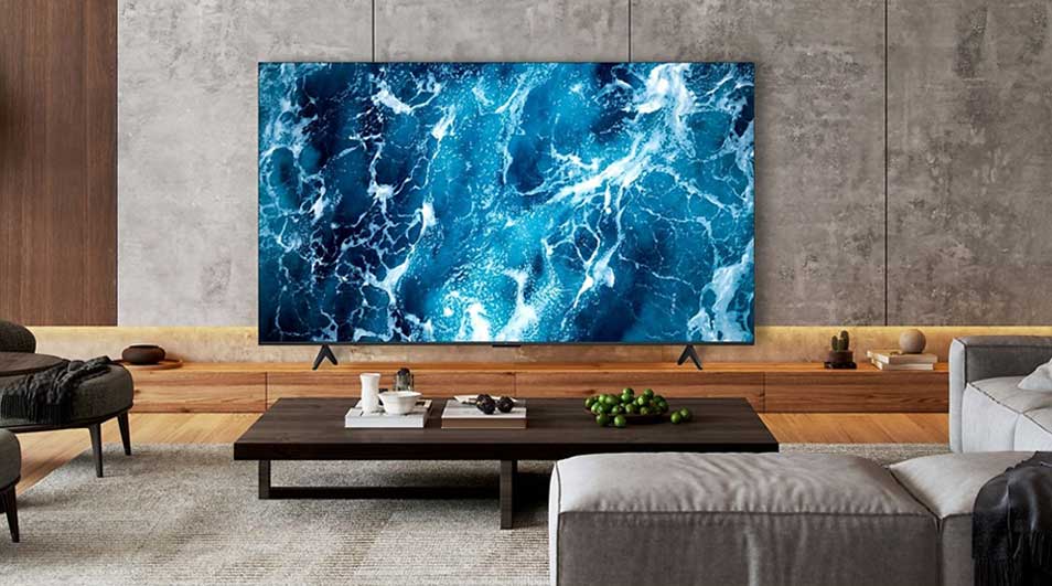 Une grande télé affiche une image abstraite bleue évoquant la mer, dans un salon élégant avec table basse, canapé et bois.