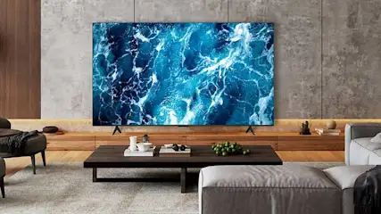 Une grande télé affiche une image abstraite bleue évoquant la mer, dans un salon élégant avec table basse, canapé et bois.