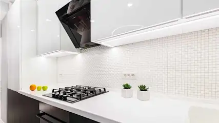 Een moderne keuken met witte tegels, een zwart gasfornuis, twee plantenpotten en enkele vruchten op het aanrecht.