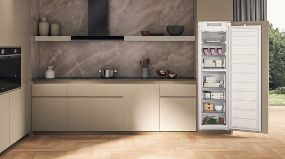 Cuisine moderne avec armoires beiges, plan de travail gris, et frigo ouvert montrant des aliments. Sol en bois clair.