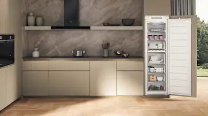 Cuisine moderne avec armoires beiges, plan de travail gris, et frigo ouvert montrant des aliments. Sol en bois clair.