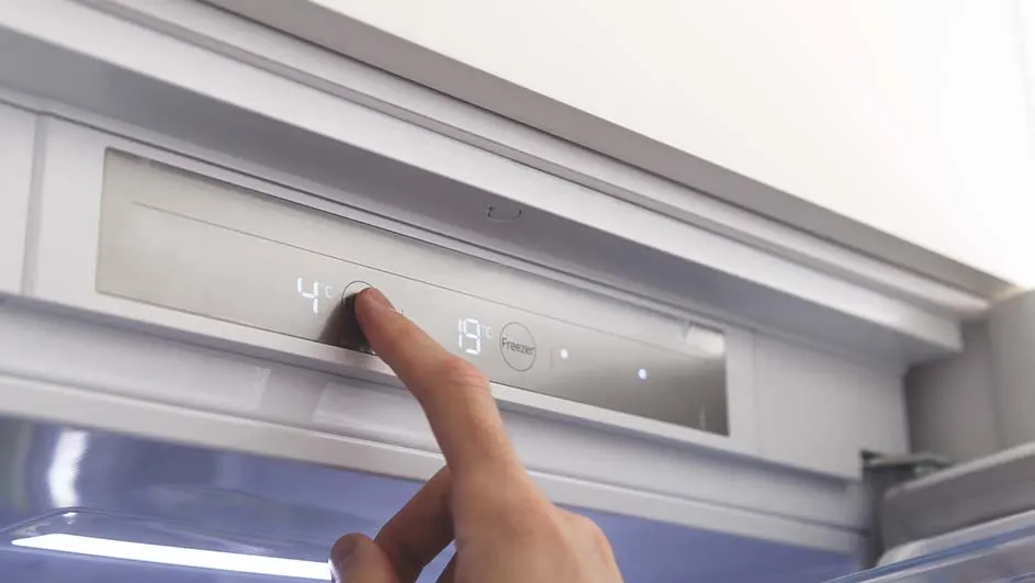 Een vinger drukt op een knop op een grijze koelkastbediening met digitale nummers "4" en "19" en het woord "Freezer".