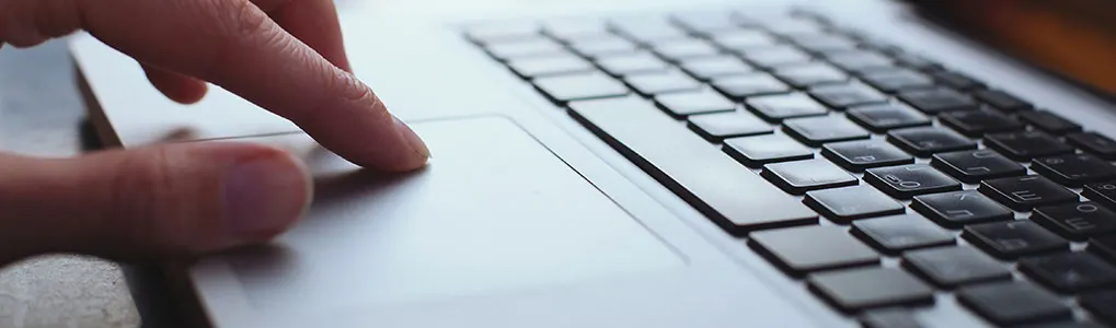 Gros plan d'un doigt sur le pavé tactile d'un ordinateur portable argenté, avec un clavier noir visible.