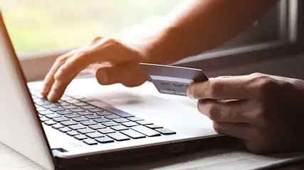Une personne utilise un ordinateur portable tout en tenant une carte de crédit. Un clavier est visible.