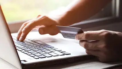 Een laptop met een hand op het toetsenbord en een creditcard wordt vastgehouden.