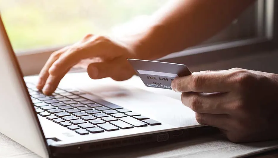 Een laptop met een hand op het toetsenbord en een creditcard wordt vastgehouden.
