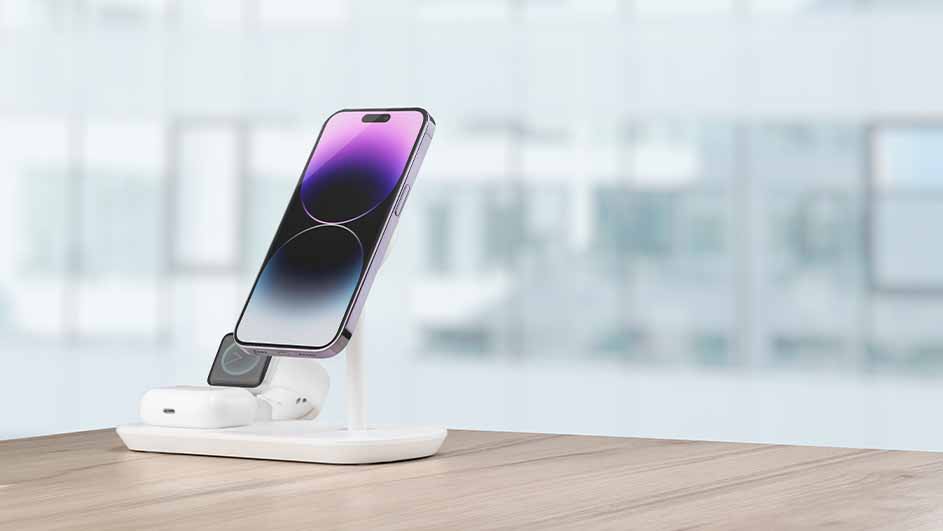 Un téléphone violet sur un support de charge blanc, avec des écouteurs et une montre, sur une table en bois.