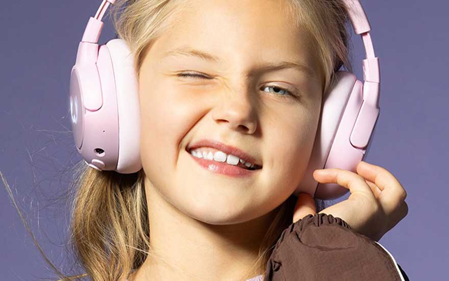 Une jeune fille portant un casque rose fait un clin d’œil malicieux à la caméra, souriant en écoutant sa musique sur un fond violet.