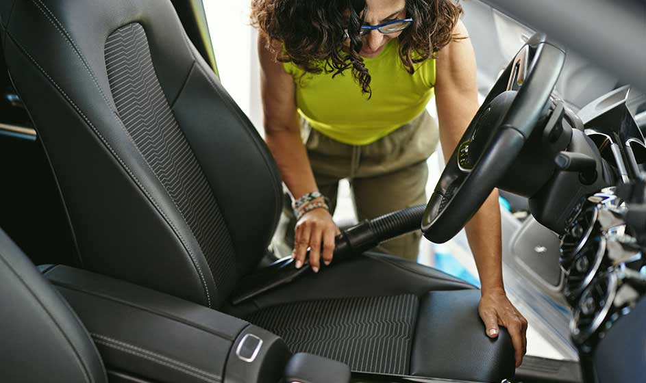Une femme aspire le siège conducteur d’une voiture ; l’intérieur paraît soigné, moderne et montré en gros plan.