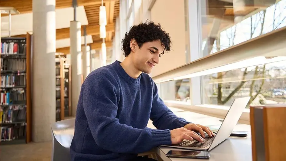 Een laptop op een tafel, met een raam en een boekenkast op de achtergrond.