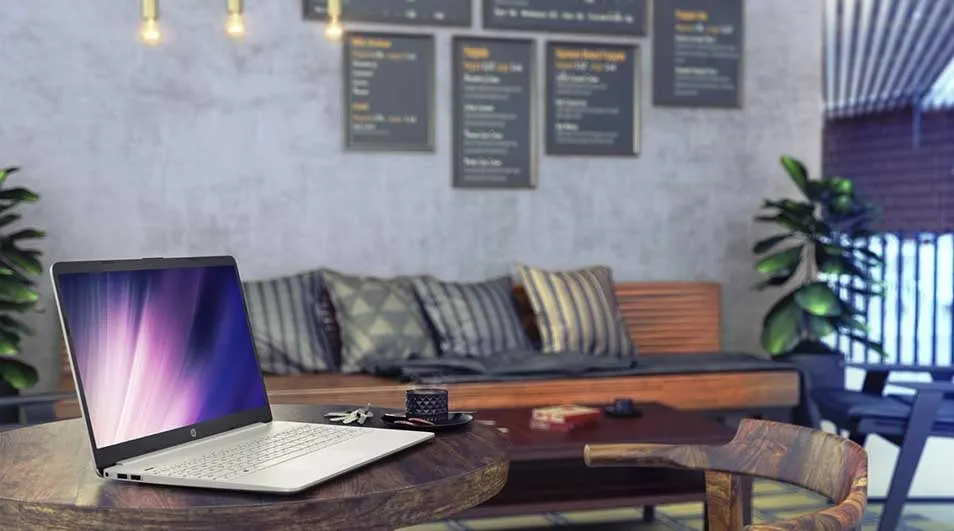 Een zilverkleurige laptop op een houten tafel in een café, met menu's aan de muur en een bank met kussens op de achtergrond.