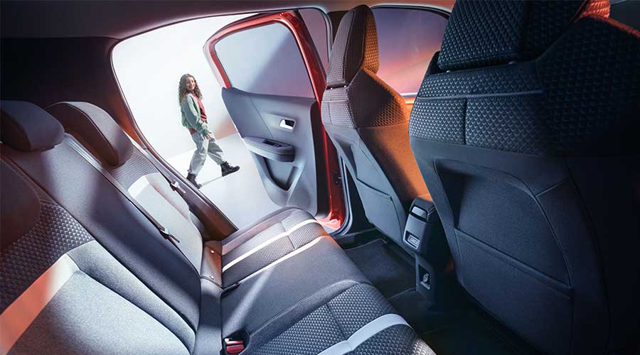 Banquette arrière spacieuse d’une voiture avec porte ouverte ; une personne passe à l’extérieur.