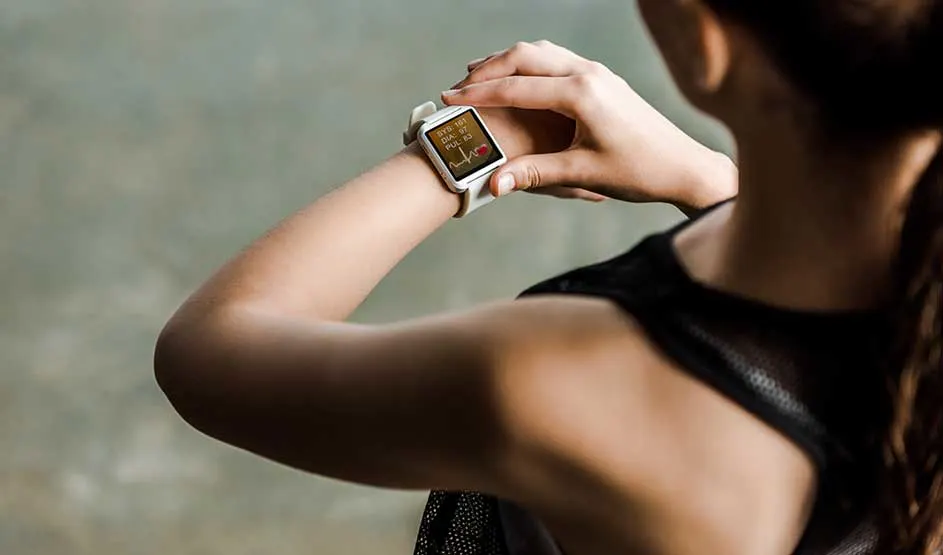 Een vrouw kijkt op haar smartwatch naar gezondheidswaarden, terwijl ze sportkleding draagt in een rustige omgeving.