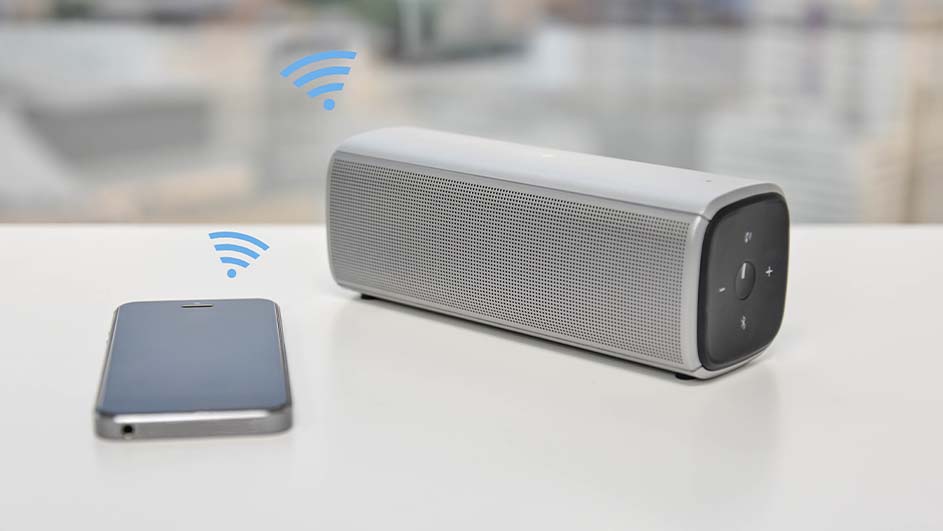 Un téléphone gris à côté d'un haut-parleur gris et noir sur une table blanche, avec des icônes Wi-Fi bleues.