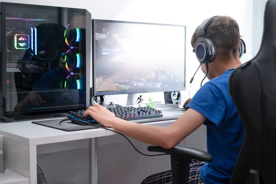 Zicht op een bureau met een computer, toetsenbord, muis en een zwart gaming-hoofdtelefoon. De pc-kast heeft gekleurde verlichting.