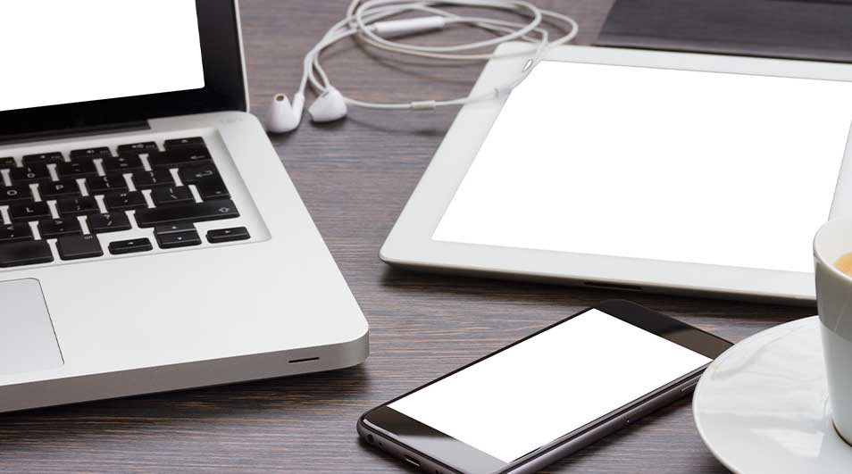 Een bureau met een laptop, tablet, smartphone, oortjes en een kop koffie. De schermen zijn wit.