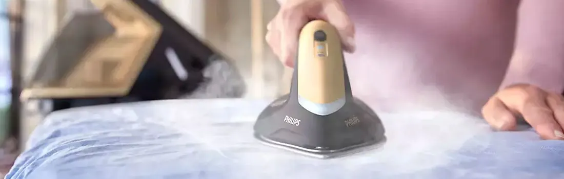 Un fer Philips gris et jaune repasse un tissu bleu clair sur une planche à repasser, avec un autre fer en arrière-plan.