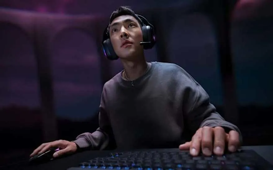 Un joueur concentré porte un casque noir avec éclairage violet en regardant vers le haut dans un environnement gaming atmosphérique.