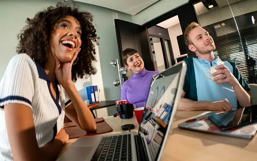 Four people sit around a table with laptops, attending a video meeting and analysing colourful graphs on the large screen.
