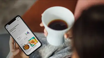 Een telefoon met een app en een witte beker met een donkere vloeistof.