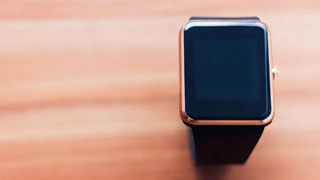 Une montre intelligente noire avec un boîtier doré repose sur une surface en bois clair.