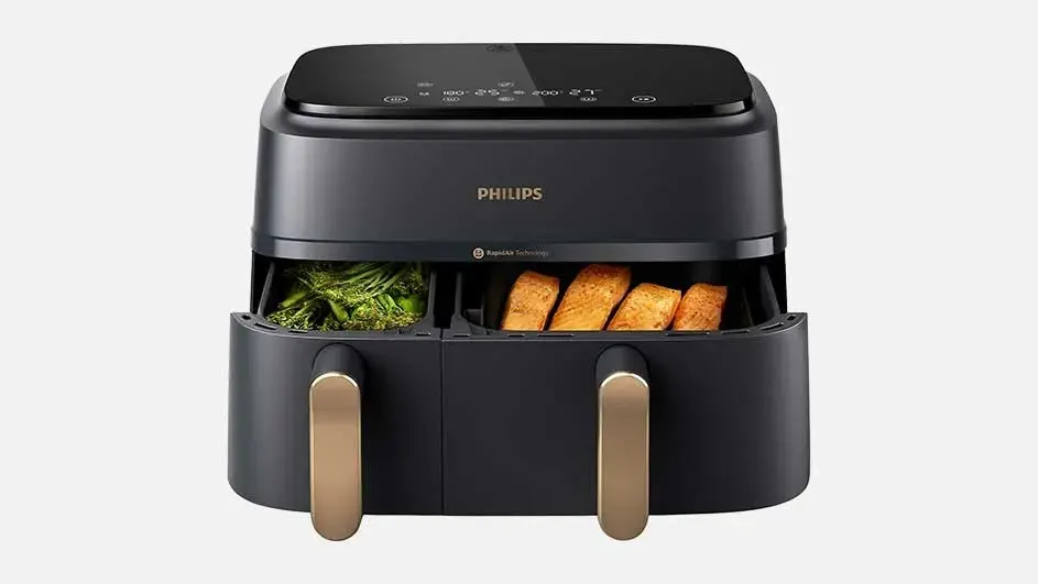 A black Philips air fryer with two drawers, veggies on the left and bread pieces on the right, sits on a white background.