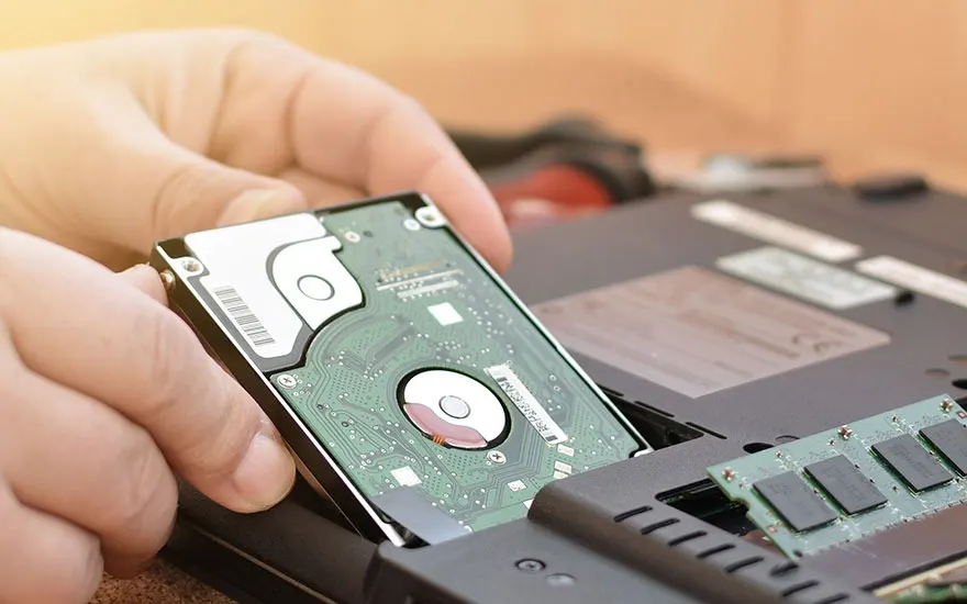 Een harde schijf wordt in een laptop geplaatst, naast RAM-geheugen op een grijze ondergrond.