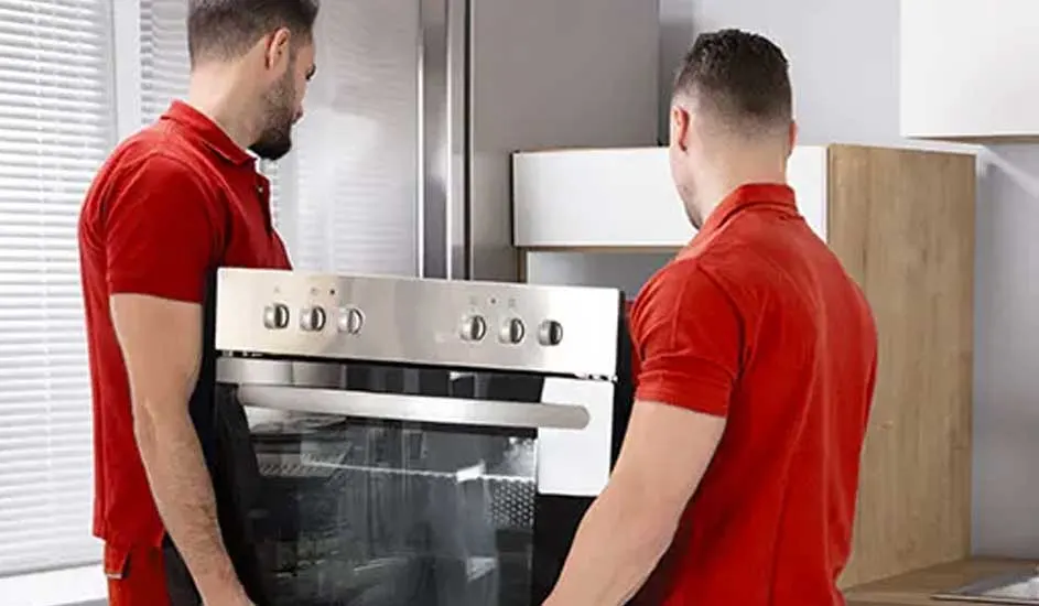 Deux personnes transportent un four en acier inoxydable dans une cuisine moderne.