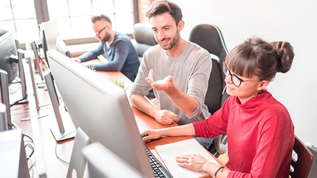 Desks avec ordinateurs dans un bureau lumineux. Ecrans gris, bureaux en bois. Personnes assises, travaillant sur des ordinateurs.